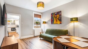 A modern apartment with a dining area, a sofa, a kitchen in the background, and a large window. - Spacious 5BR Home With Parking in Central Horsham (Horsham)