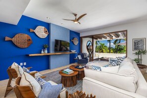 A modern living room with a blue accent wall, a ceiling fan, a flat-screen TV, a sofa, and a coffee table. - Punta Mita 4 Bedrooms 4 5 Baths Golf Course Views Casa Azul Bahia 22 (Punta de Mita)