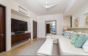 A modern living room with a flat-screen TV, a ceiling fan, a sofa with patterned cushions, a patterned rug, and a large mirror. - Casa Sole in Punta Mita (Punta de Mita)