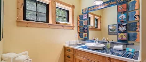 Un baño con armarios de madera, un lavamanos, una ventana y un espejo con ilustraciones motivacionales.