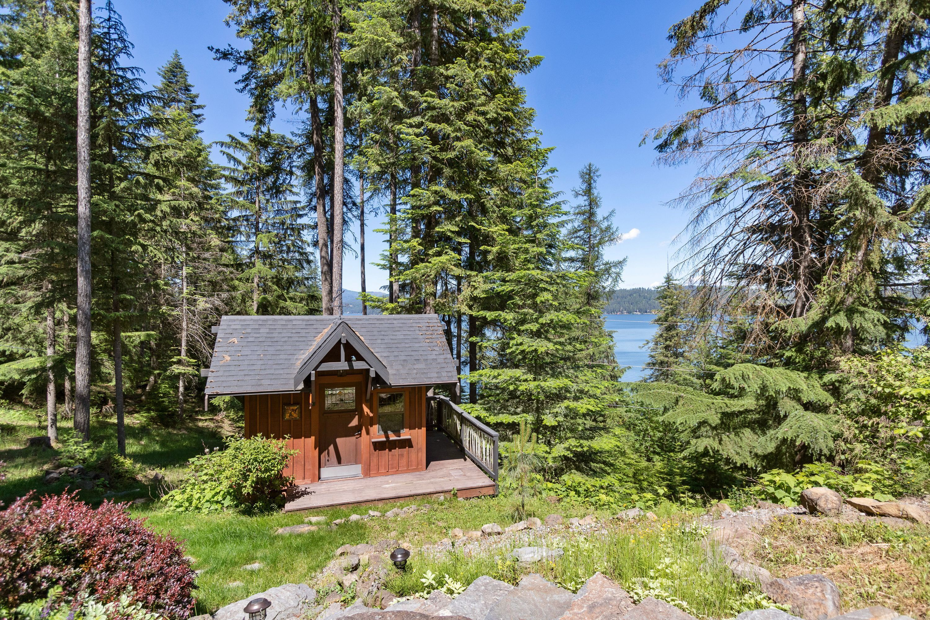 A cabin with a deck, surrounded by dense forest and a lake view.