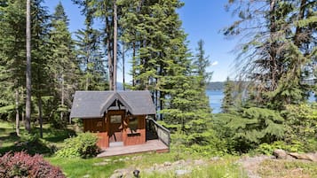 A cabin with a deck, surrounded by dense forest and a lake view.