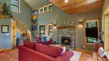 A cozy living room with a fireplace, a red sofa, a wooden staircase, and a stone fireplace surround.