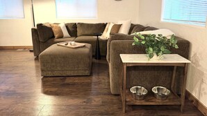 Un salon comprenant un canapé, un pouf, une table d’appoint avec des bols, une horloge et une plante.