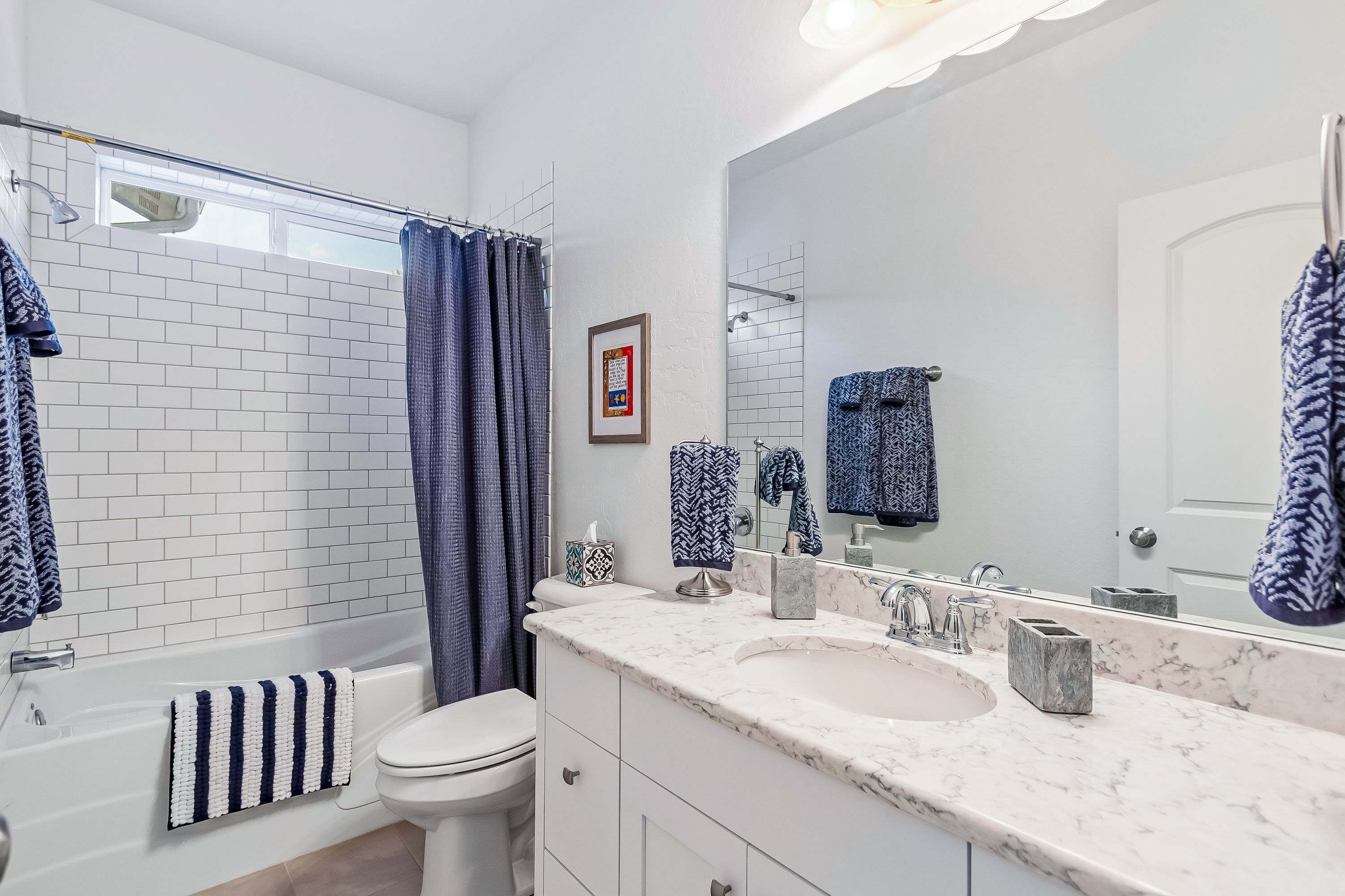 A bathroom with a white bathtub, a white toilet, a large mirror, and a marble countertop with a sink.