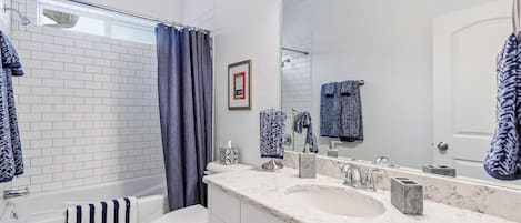 A bathroom with a white bathtub, a white toilet, a large mirror, and a marble countertop with a sink.