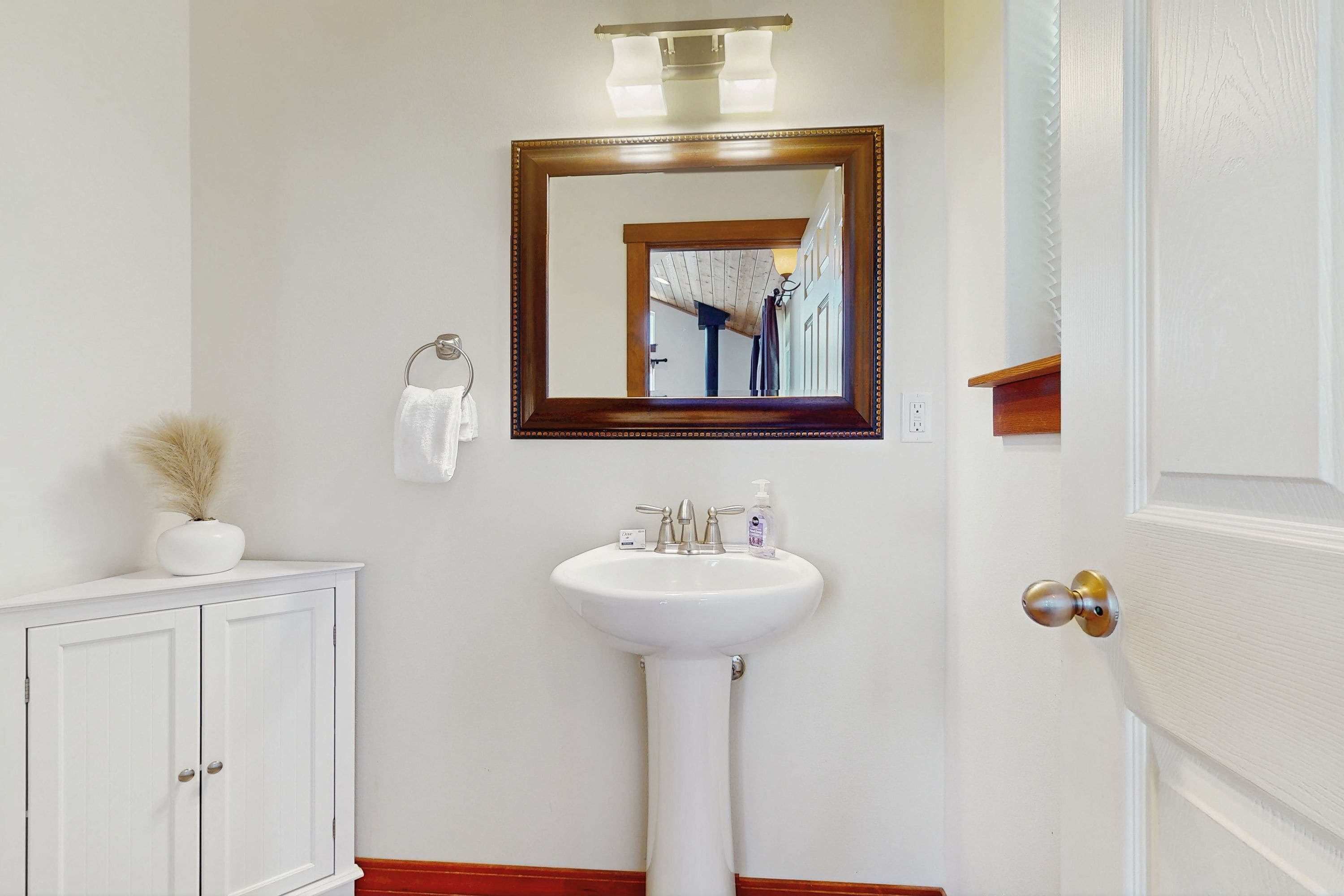 A bathroom with a white sink, a mirror with a wooden frame, a towel rack, and a cabinet.