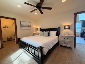 A bedroom with a bed, two bedside tables with lamps, a ceiling fan, a painting on the wall, and a view of the outside balcony. - Lakeside Hideaway in Harrison (Harrison)