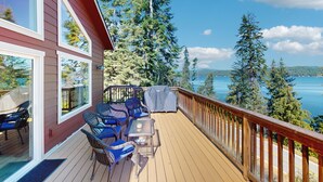 A deck with outdoor furniture, a barbecue, and a view of a lake and forest.