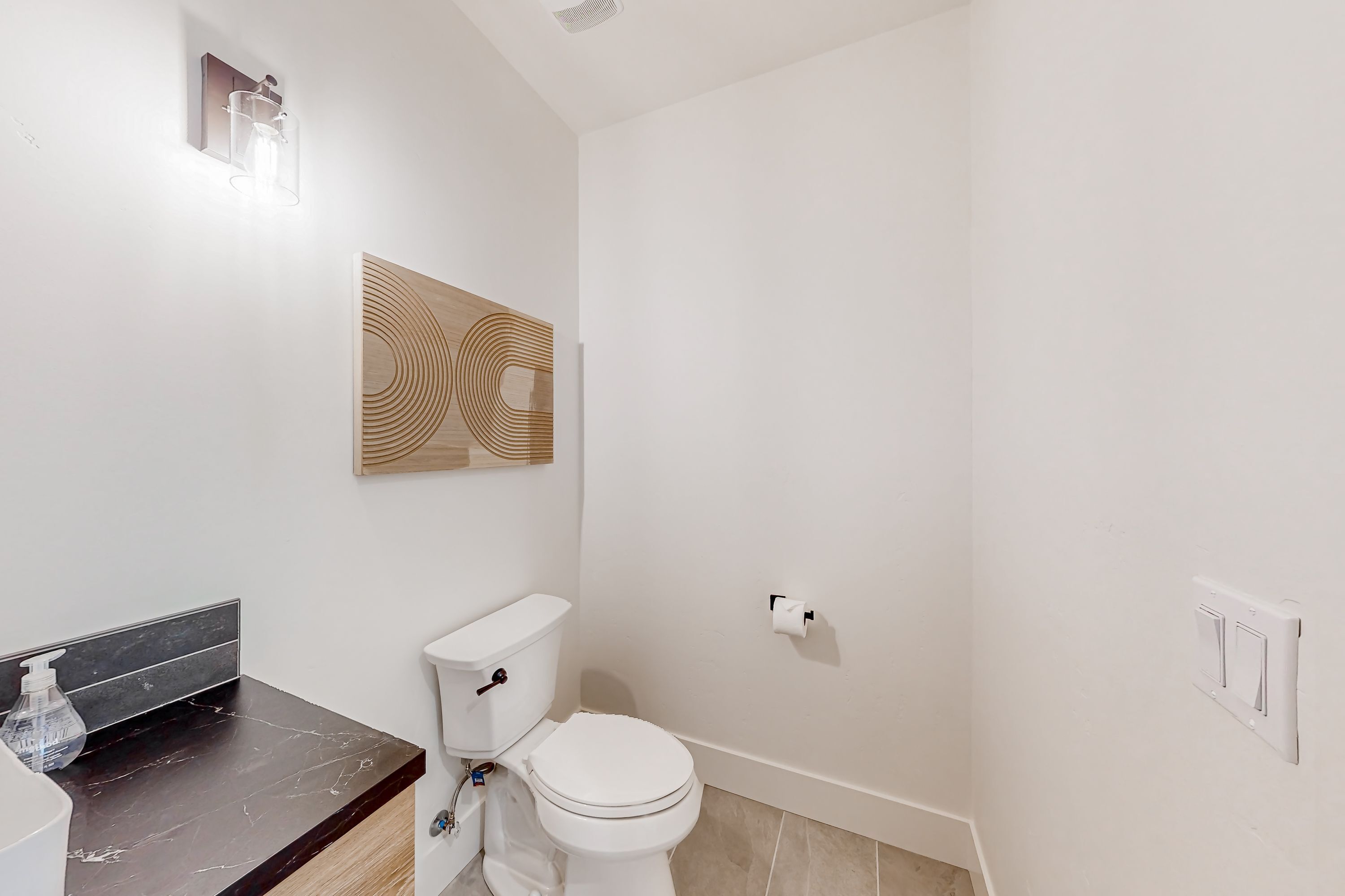 Une salle de bain moderne comprenant des toilettes, un lavabo avec un plan de travail en marbre, un luminaire fixé au mur et un panneau décoratif en bois.