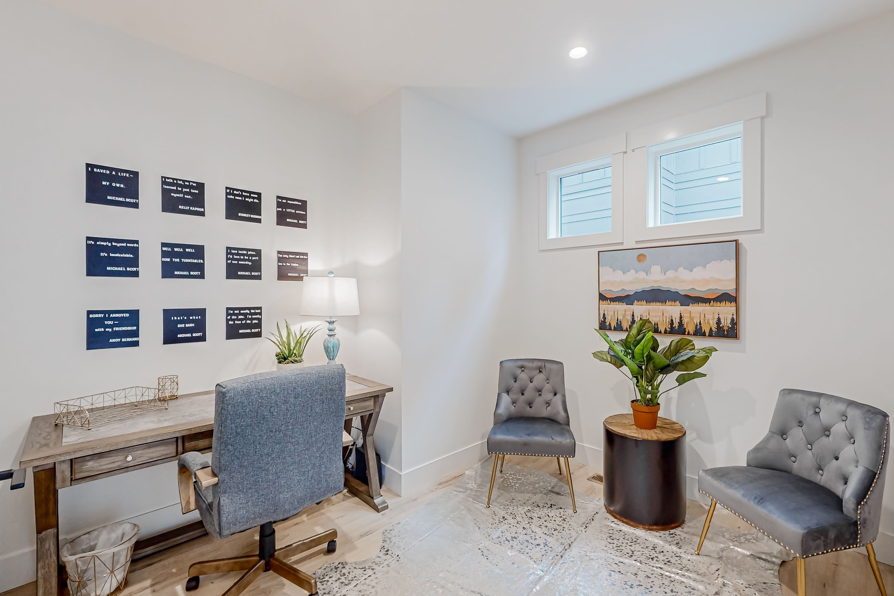 A modern office space with a desk, two chairs, a potted plant, and a wall with framed quotes.