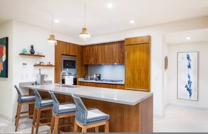Eine moderne Küche mit Holzausstattung, einer zentralen Kochinsel mit Barhocker und Pendelleuchten.