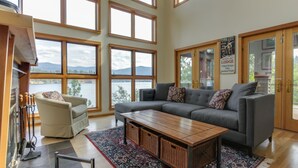 A spacious living room with a large gray sofa, a wooden coffee table, and a view of the lake through large windows.