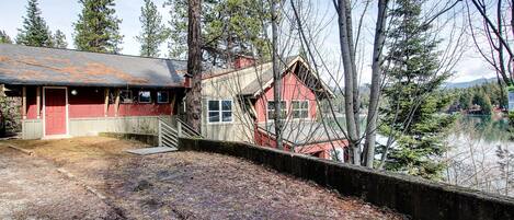 Un chalet rustique à l’extérieur rouge, doté d’une terrasse en bois et offrant une vue sur un lac.