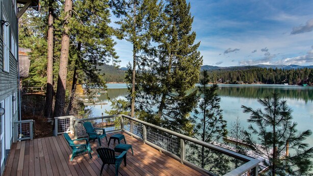 A wooden deck with chairs, overlooking a lake with trees and mountains in the background.