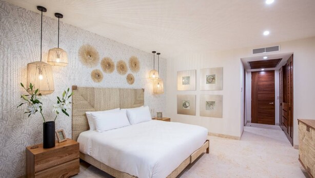 Un dormitorio con cama, mesitas de noche, decoración en la pared y una puerta que da a otra habitación.