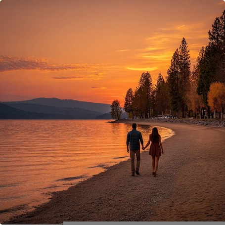 A couple walking on a pebbled beach with a sunset in the background.