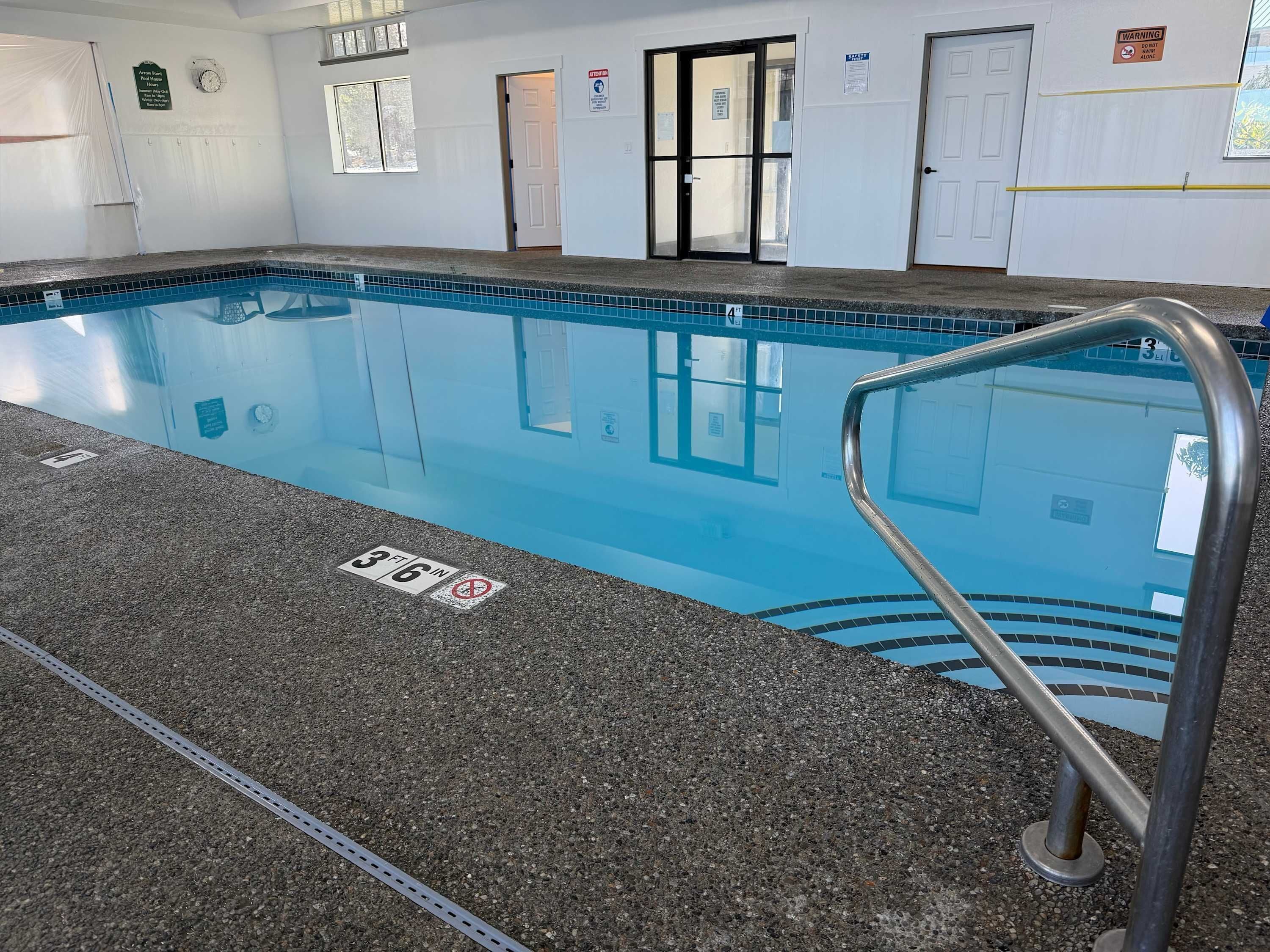 An indoor swimming pool with a clear water surface, marked depth lines, and a metal pool ladder.