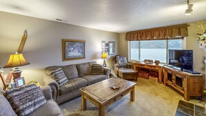 Una sala de estar con sofá, mesa de centro, televisor y vistas al exterior.