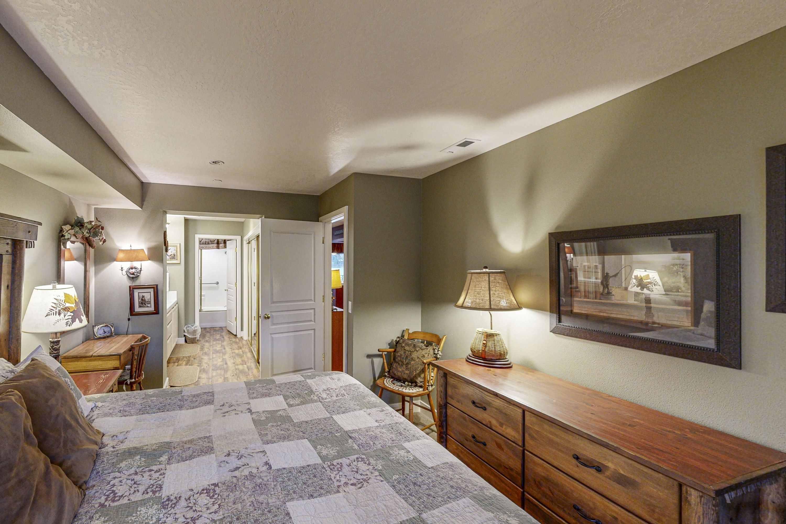 A bedroom with a bed, dresser, chair, lamp, and framed picture on the wall.