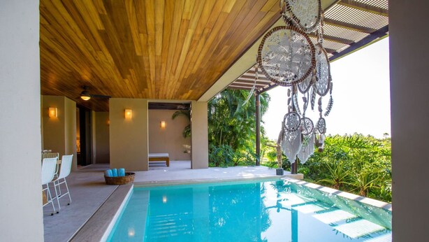 Un área de piscina moderna con techo de madera, una banca y un adorno de atrapasueños.