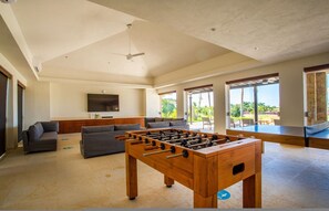 A spacious living area with a foosball table, sofas, and a television. - 3 bd Condo With Ocean Views HK (San Marcos)