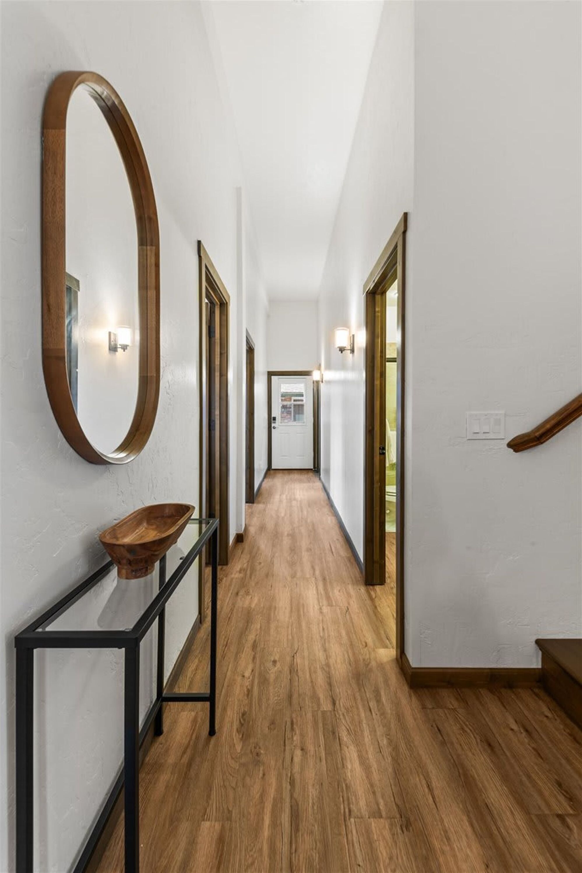 A hallway with wooden flooring, a round mirror, and a console table.