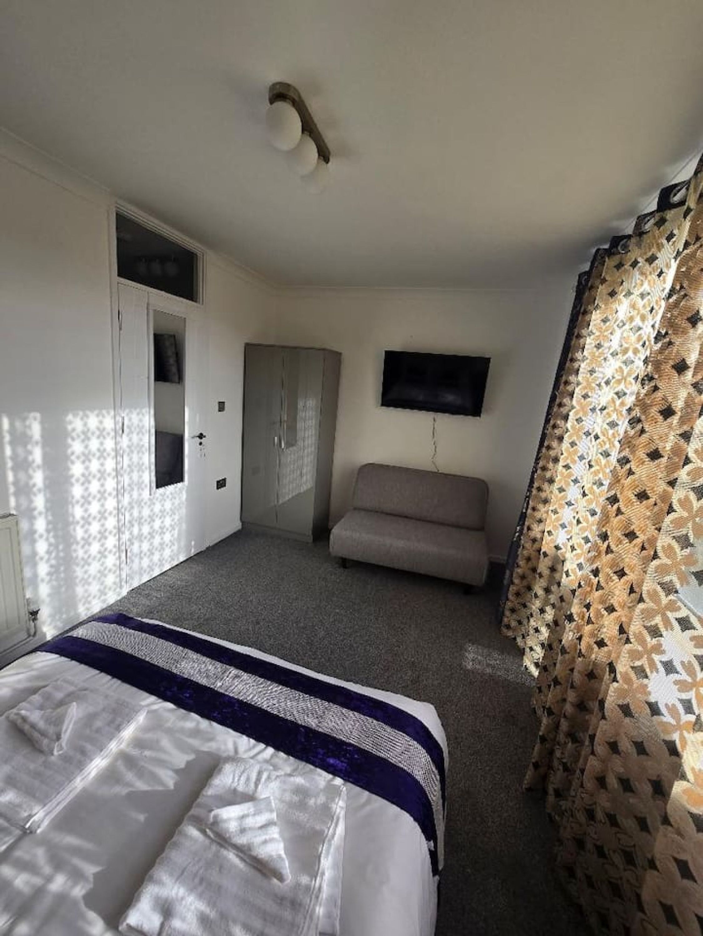 Een hotelkamer met een bed, een bank, een televisie en een gordijn met een patroon.
