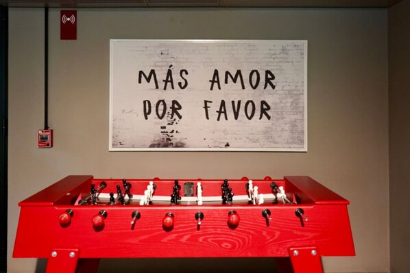 A red foosball table in front of a wall with a sign that reads 'MÁS AMOR POR FAVOR'. - Naya 1202 Tower I in Punta de Mita (Punta de Mita)