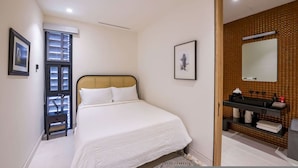 A bedroom with a bed, a nightstand, a window with blinds, a framed picture on the wall, and a bathroom with a sink and mirror. - Naya 1202 Tower I in Punta de Mita (Punta de Mita)