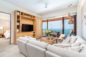 A modern living room with a large flat-screen TV, a sofa, a coffee table, and a view of the sea through large windows. - Luxury 4 bed 4 Bath Beach Front Condo - Bucerias (Bucerías)
