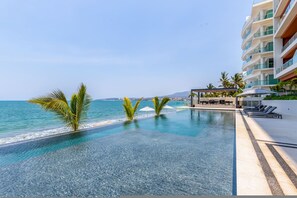 A resort pool with a view of the ocean, palm trees, and a building with balconies. - Luxury 4 bed 4 Bath Beach Front Condo - Bucerias (Bucerías)