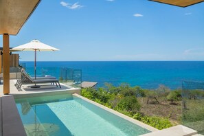 A pool with a glass barrier, lounge chairs, and an umbrella, overlooking a clear blue sea. - 4 bd Beach Chic Villa Ocean View - Iyari B4 (Punta de Mita)
