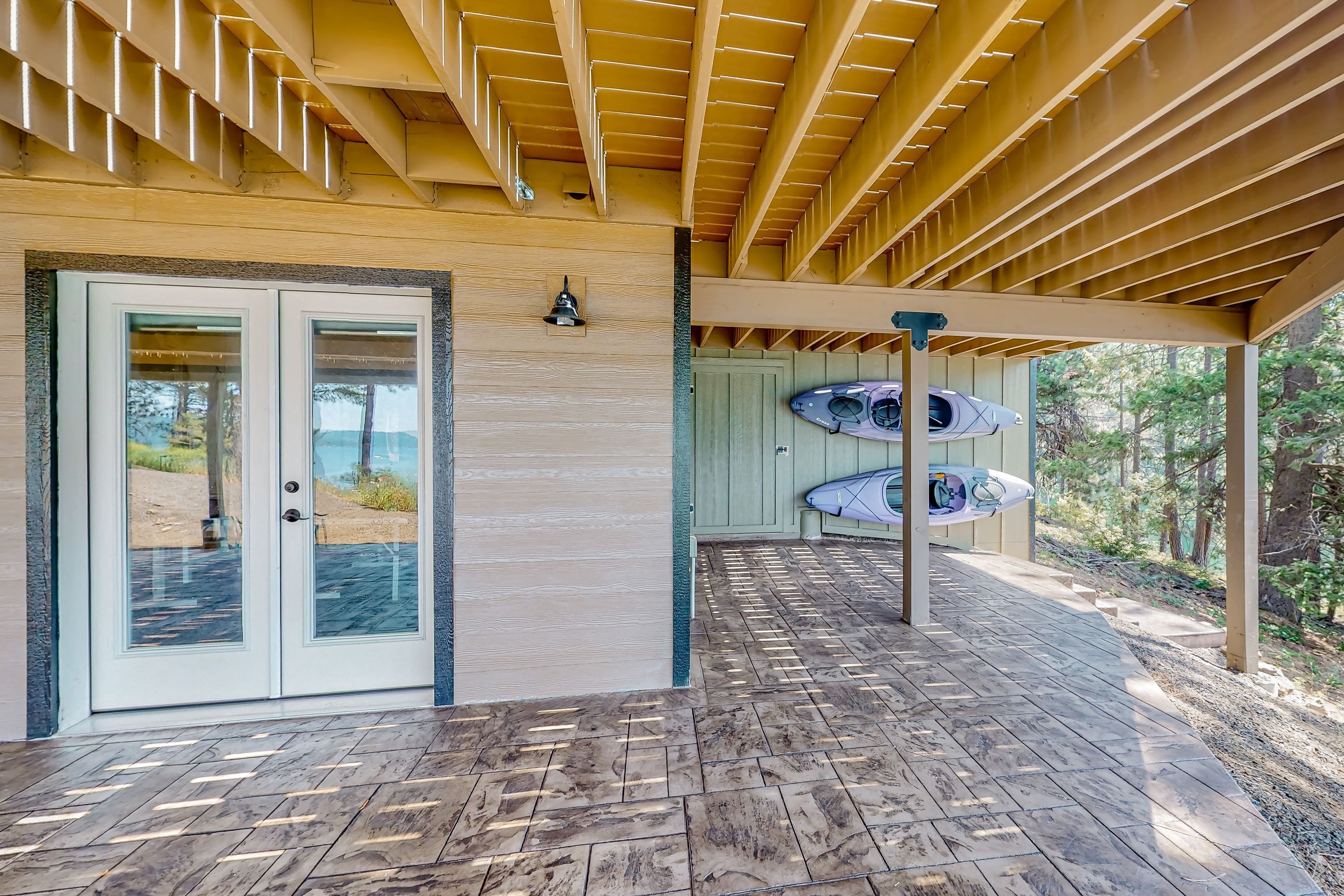 Un patio cubierto con techo de madera, una puerta de vidrio y kayaks colgados en una pared.