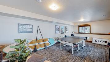 Una habitación con mesa de ping pong, tablas de surf y cuadros en las paredes.
