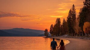 Un couple se promène sur une plage de galets, avec un coucher de soleil en arrière-plan.