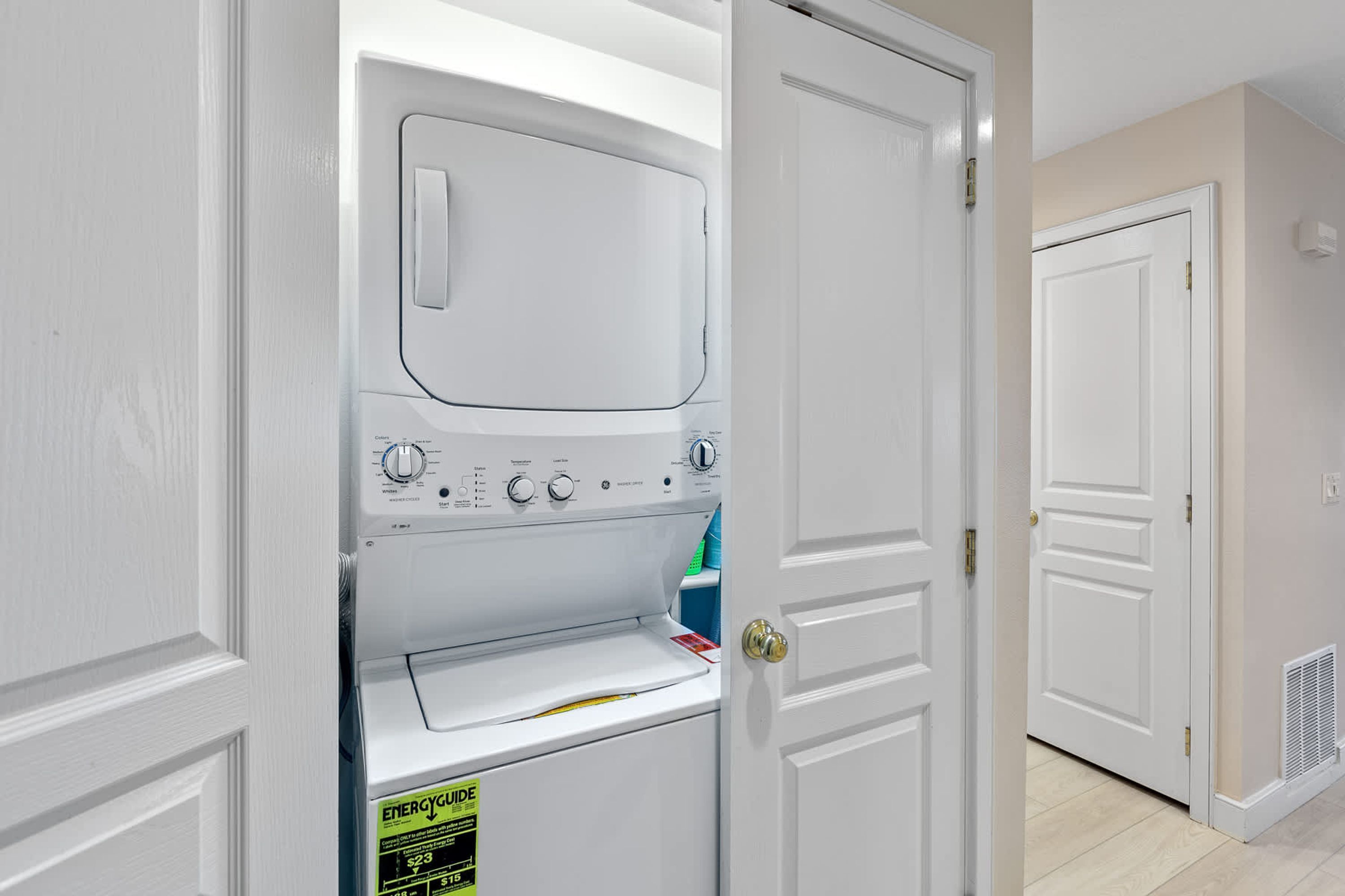 Une buanderie équipée d’un lave-linge et d’un sèche-linge à chargement frontal, d’une porte avec une poignée en laiton et d’une porte blanche en arrière-plan.