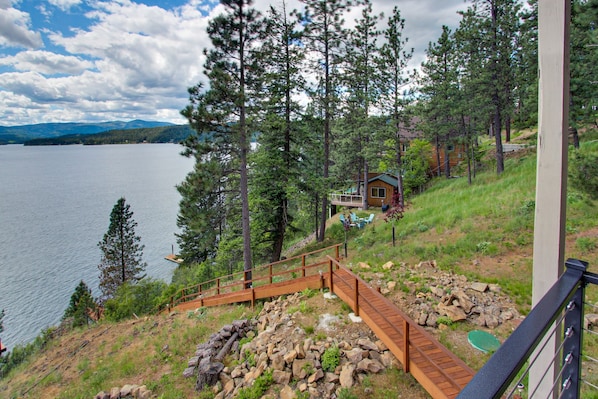 A cabin by a lake with a wooden deck, surrounded by trees. - Perfect Panoramic Paradise (Harrison)