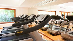 Ein Fitnessstudio mit mehreren Laufbändern, Holzboden und großen Fenstern mit Blick auf Grünflächen.