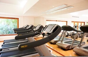Ein Fitnessstudio mit mehreren Laufbändern, Holzboden und großen Fenstern mit Blick auf Grünflächen.