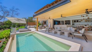 Et moderne poolområde med liggestole og en overdækket terrasse.