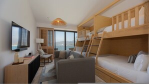 Et lille hotelværelse med køjeseng, skrivebord med lampe, stol og fjernsyn.