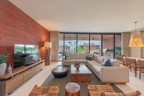 Ein modernes Wohnzimmer mit großem Flachbildfernseher, einer Couch, einem Couchtisch und einem Essbereich mit Holzsesseln und einem Tisch.