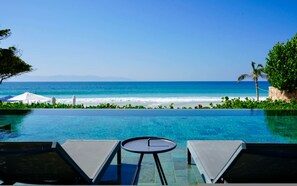 Ein Pool mit Blick auf den Ozean, zwei Liegestühle und ein kleiner Tisch.