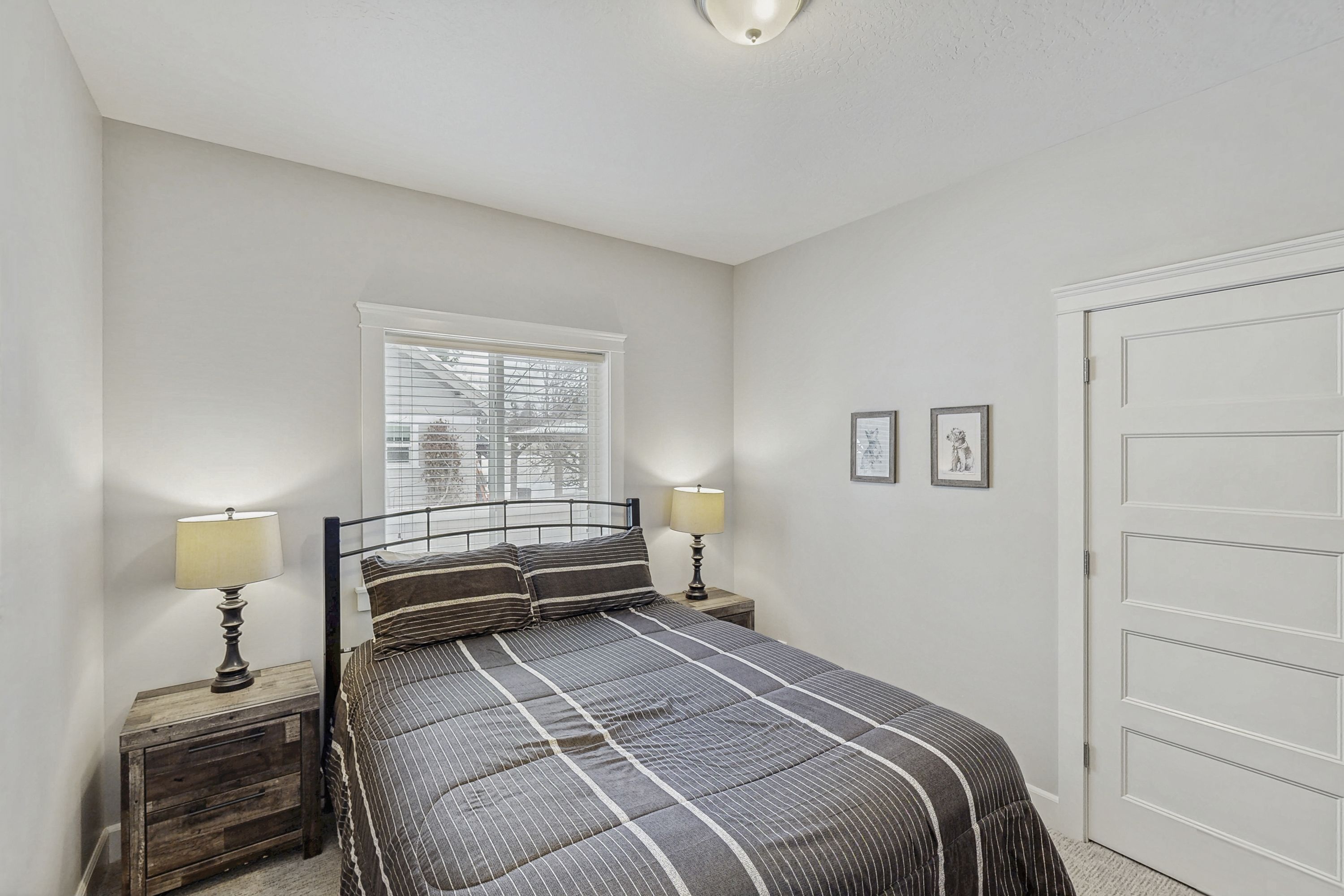 A bedroom with a bed, two bedside tables with lamps, a window, and a door.