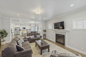 A living room with a sofa, coffee table, fireplace, TV, and kitchen in the background. - 6th Street Retreat in Coeur d Alene (Coeur d'Alene)