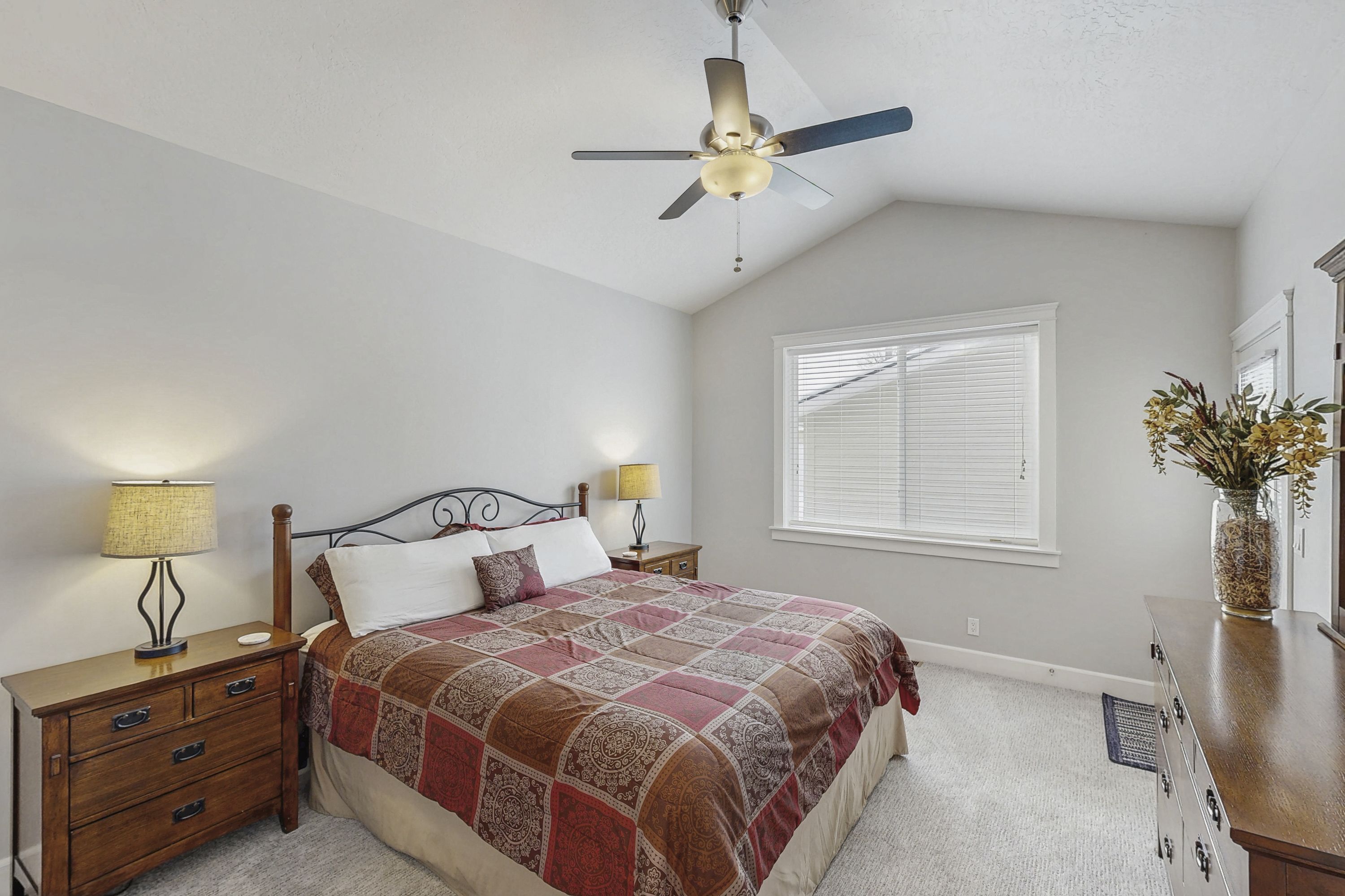 A bedroom with a bed, nightstands, a ceiling fan, a window with blinds, and a dresser.