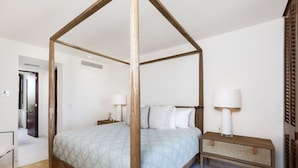 Ein Bett mit Baldachin, eine steckbare Bettdecke mit Muster, ein Nachttisch mit Lampe und ein gewebter Beistelltisch.