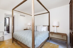 A four-poster bed with a patterned bedspread, a bedside table with a lamp, and a woven side table. - Las Marietas D101 Punta Mita Private Pool (Punta de Mita)