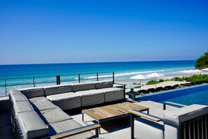 A poolside area with a sofa, a wooden table, and lounge chairs. - Naya 6401 Tower VI in Bahia de Banderas (Punta de Mita)
